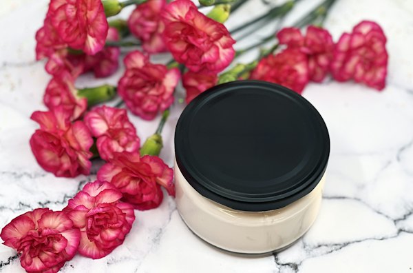 A jar of cream on marble with carnations